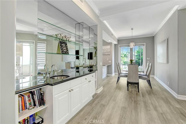 kitchen with ornamental molding, sink, light hardwood / wood-style flooring, white cabinets, and hanging light fixtures