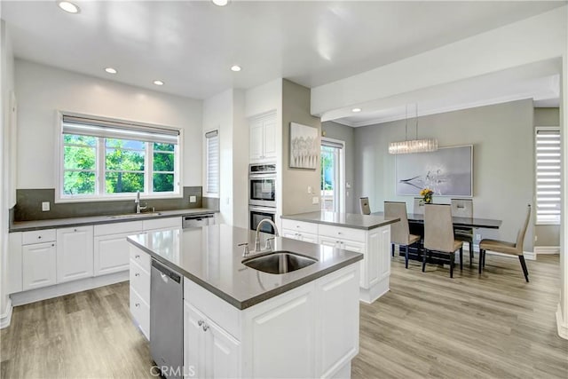 kitchen featuring pendant lighting, sink, white cabinetry, and an island with sink