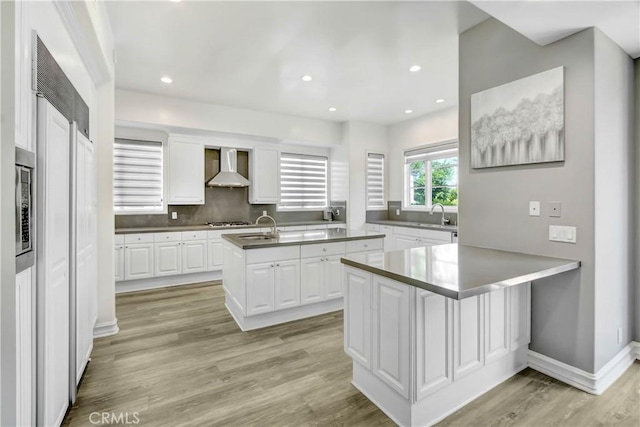 kitchen with white cabinets, light hardwood / wood-style floors, a kitchen island with sink, and wall chimney exhaust hood