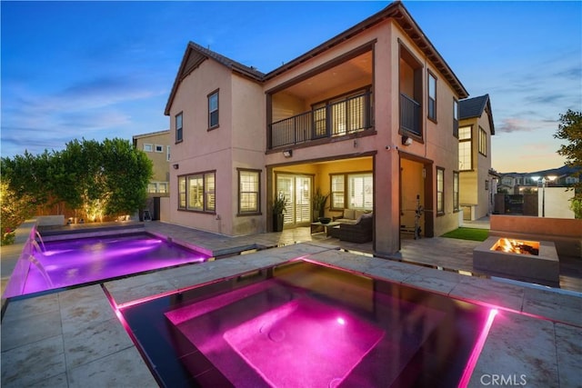 pool at dusk with pool water feature, a patio area, an in ground hot tub, and an outdoor living space with a fire pit