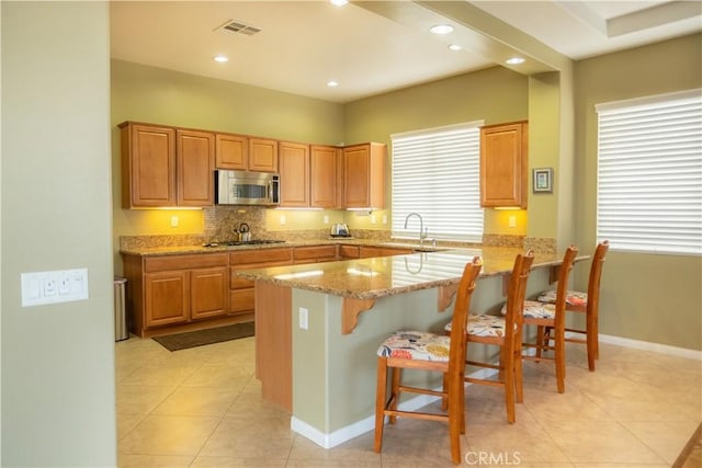 kitchen featuring light stone countertops, stainless steel appliances, sink, light tile patterned floors, and a breakfast bar area