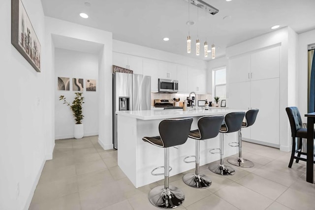 kitchen featuring stainless steel appliances, tasteful backsplash, a kitchen island with sink, pendant lighting, and white cabinets