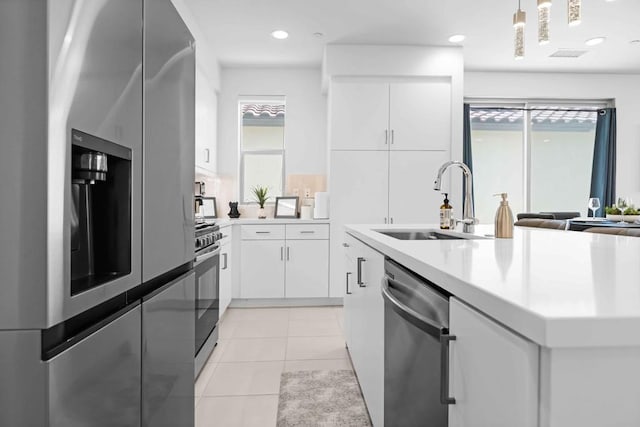 kitchen featuring decorative light fixtures, white cabinetry, stainless steel appliances, sink, and light tile patterned floors