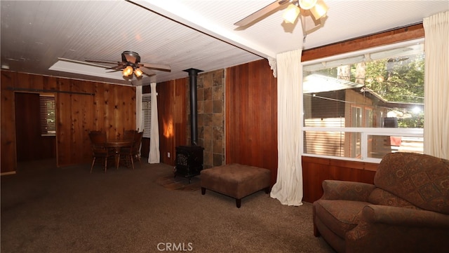 interior space with ceiling fan, wooden walls, and a wood stove