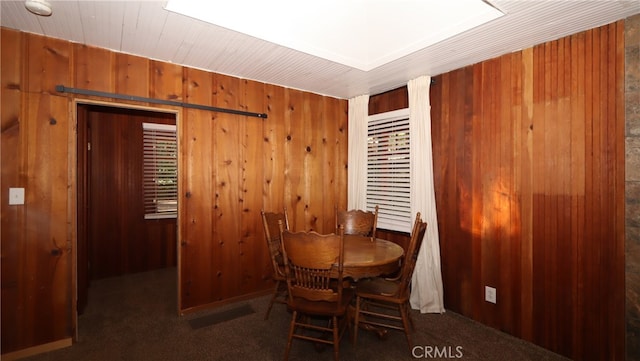 dining space featuring wood walls and dark carpet