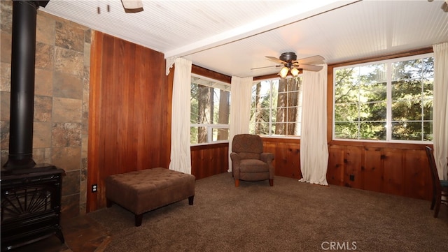 sunroom / solarium featuring ceiling fan, plenty of natural light, beam ceiling, and a wood stove