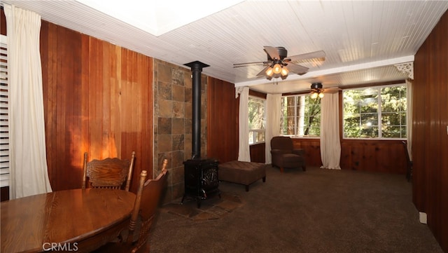 interior space featuring ceiling fan, wood walls, dark colored carpet, and a wood stove