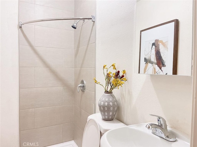 bathroom with tiled shower, toilet, and sink