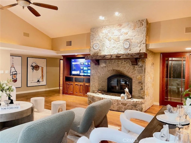 living room with ceiling fan, a stone fireplace, wood-type flooring, and high vaulted ceiling