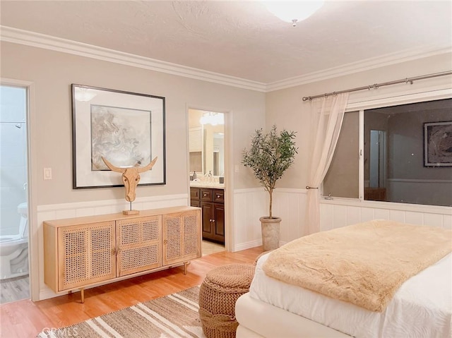 bedroom with wood-type flooring, ornamental molding, and connected bathroom