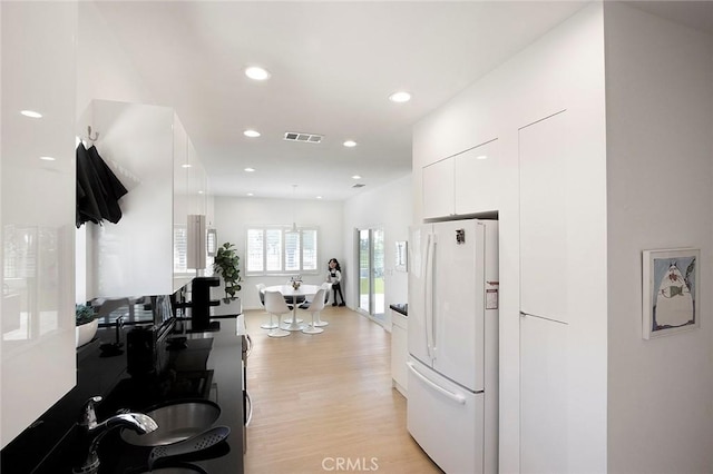 kitchen with white cabinetry, white fridge, and light wood-type flooring