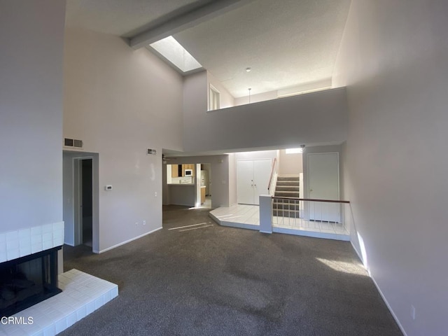 unfurnished living room with a skylight, a fireplace, dark colored carpet, high vaulted ceiling, and beam ceiling