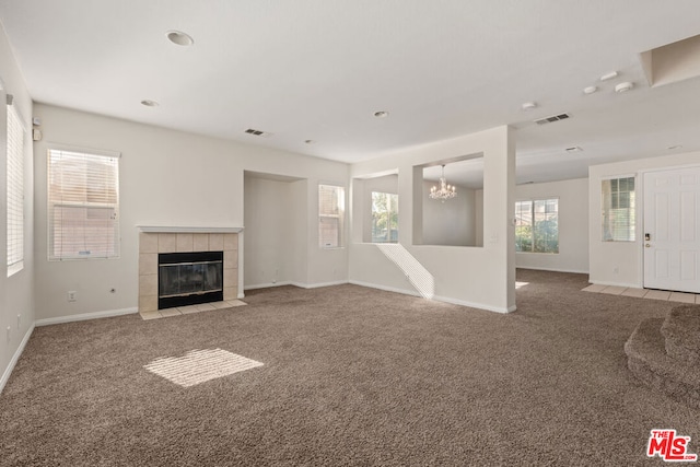 unfurnished living room with carpet floors, a notable chandelier, and a tile fireplace