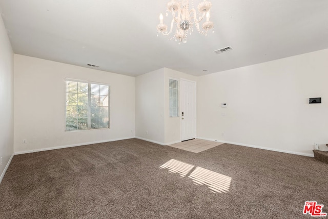 carpeted empty room with an inviting chandelier