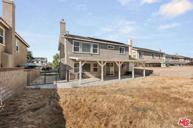 back of house with a patio area, a lawn, and solar panels