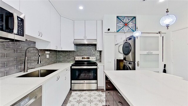 kitchen featuring hanging light fixtures, white cabinets, stainless steel appliances, stacked washer / drying machine, and sink