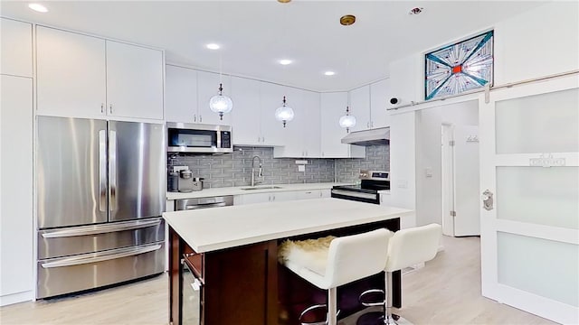 kitchen with appliances with stainless steel finishes, light countertops, white cabinetry, pendant lighting, and a sink