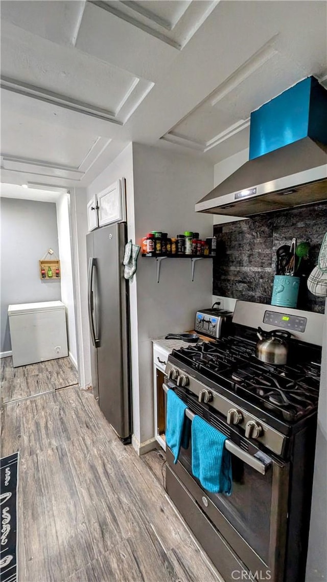 kitchen featuring light wood-type flooring, stainless steel appliances, and wall chimney range hood