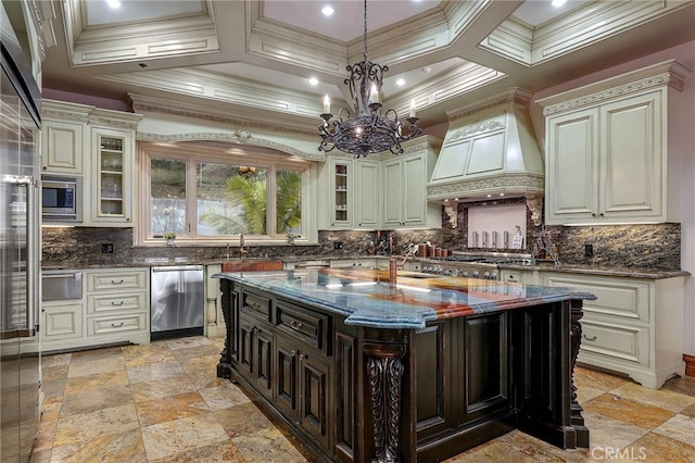 kitchen featuring premium range hood, an island with sink, stainless steel appliances, dark stone counters, and a chandelier