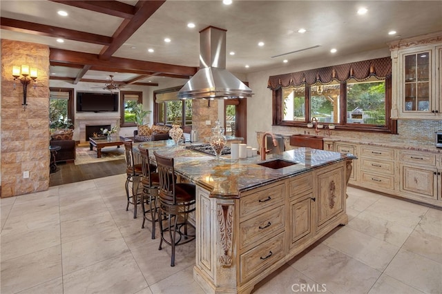 kitchen with light stone countertops, a large island with sink, beamed ceiling, sink, and a breakfast bar