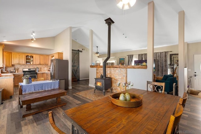 dining space featuring dark hardwood / wood-style floors, a wood stove, a barn door, high vaulted ceiling, and ceiling fan