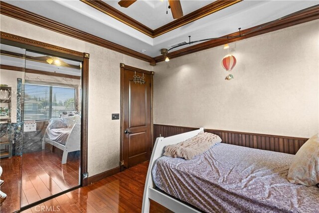 bedroom with ceiling fan, a raised ceiling, crown molding, and hardwood / wood-style floors