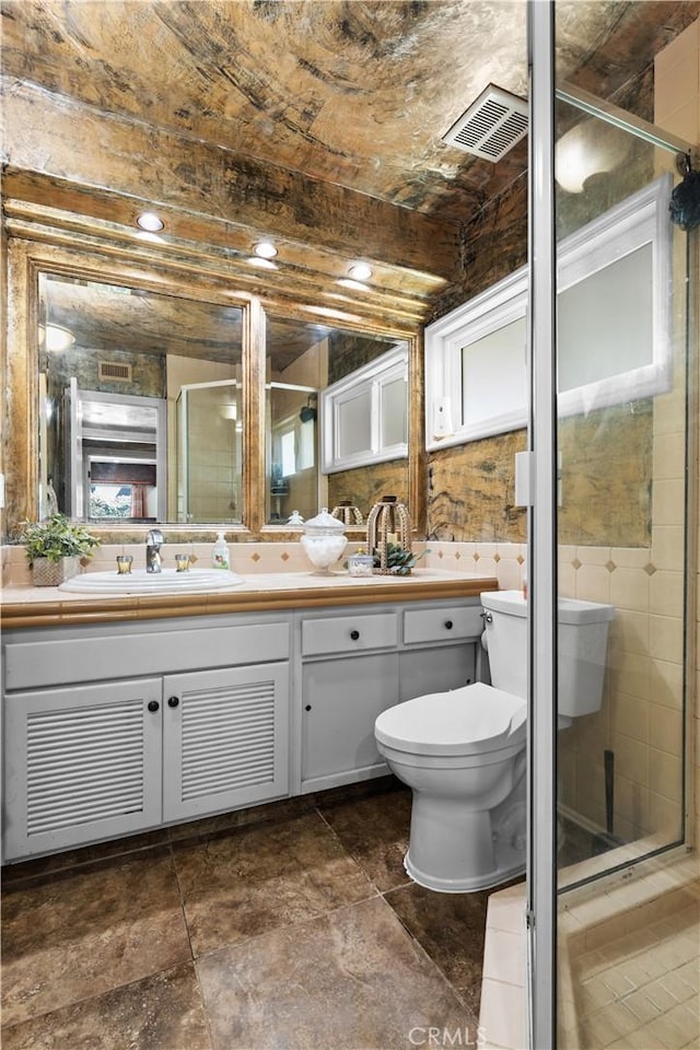 bathroom featuring toilet, vanity, tile walls, and a shower with door