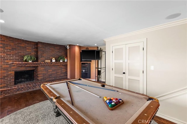 recreation room with a brick fireplace, crown molding, dark hardwood / wood-style floors, and billiards