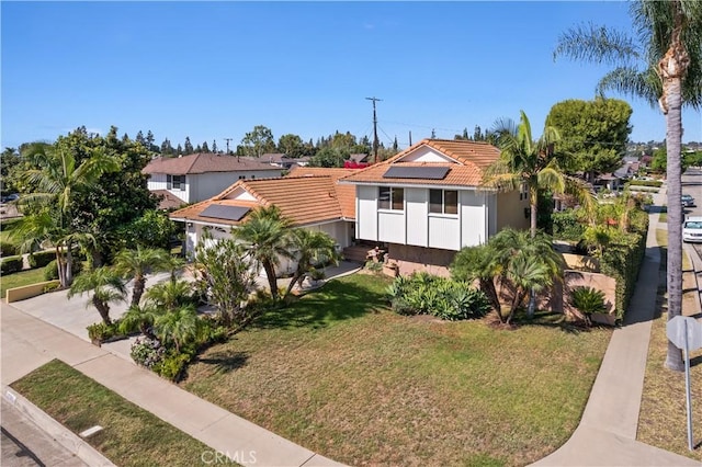 view of front of home with driveway, a tiled roof, a front lawn, and solar panels