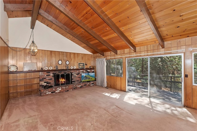 unfurnished living room featuring beamed ceiling, wood walls, a brick fireplace, carpet, and wooden ceiling