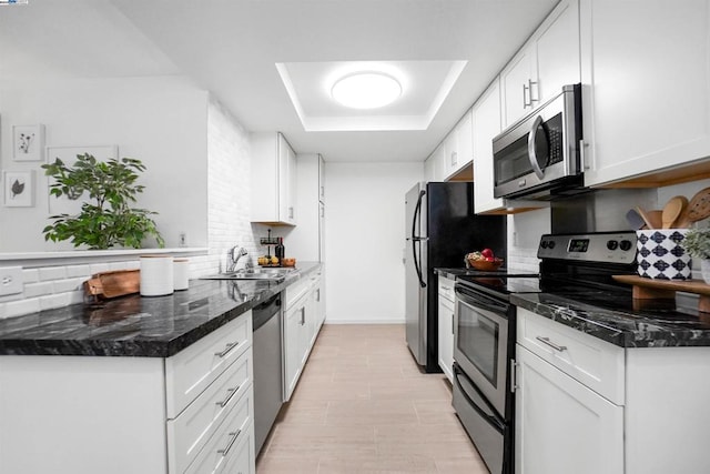 kitchen with sink, white cabinets, decorative backsplash, stainless steel appliances, and dark stone countertops