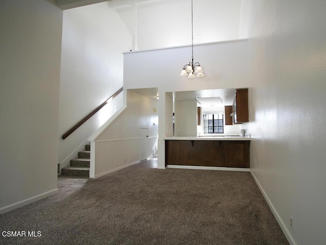 unfurnished living room with dark carpet, high vaulted ceiling, and a chandelier