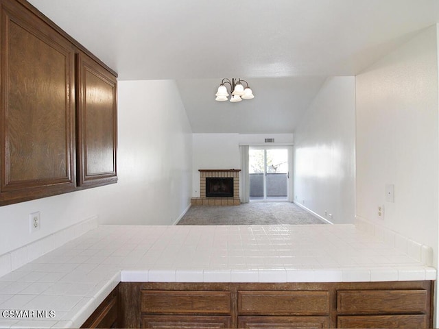 kitchen with a brick fireplace, light colored carpet, a chandelier, tile counters, and lofted ceiling