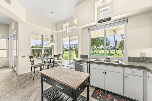 kitchen featuring dishwasher, sink, light hardwood / wood-style flooring, decorative light fixtures, and white cabinets