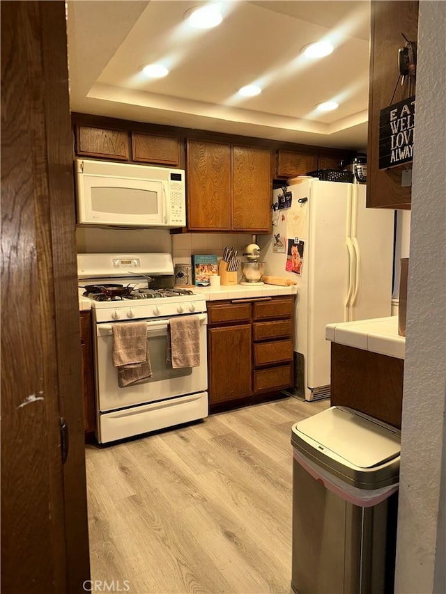 kitchen featuring a raised ceiling, white appliances, and light hardwood / wood-style flooring