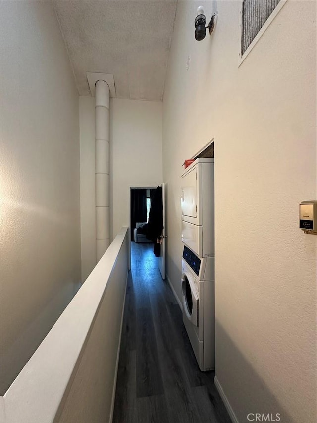 hall featuring stacked washer / dryer and dark wood-type flooring