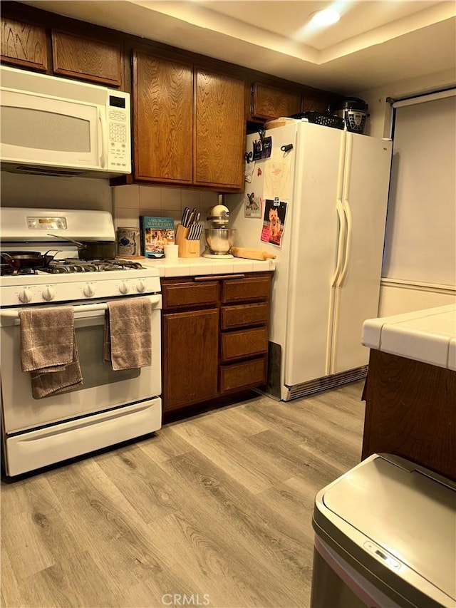 kitchen featuring tile counters, white appliances, and light wood-type flooring