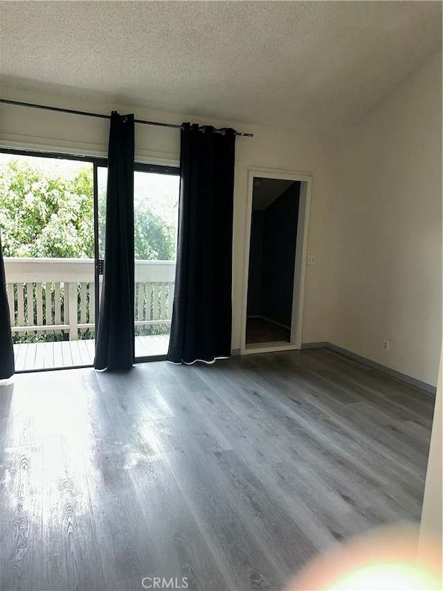 empty room featuring a textured ceiling, baseboards, and wood finished floors