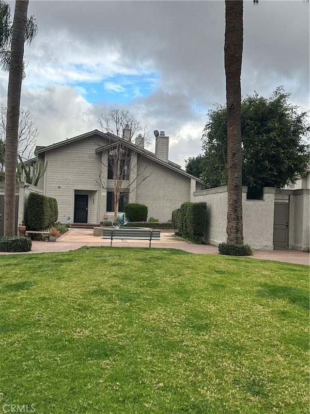 rear view of property featuring stucco siding, a lawn, a chimney, and a patio