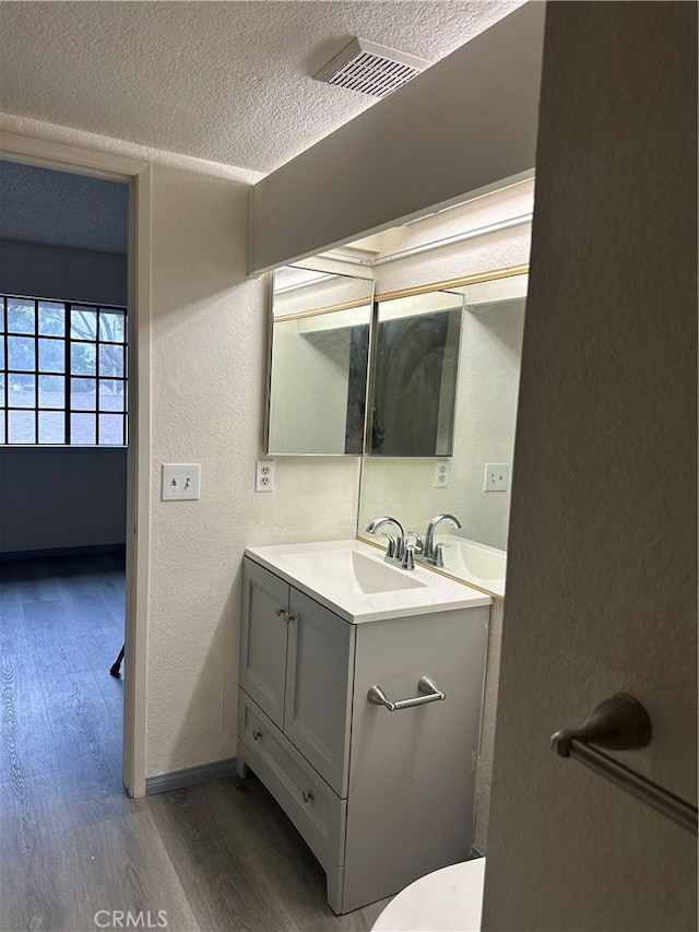 bathroom with a textured ceiling, a textured wall, wood finished floors, visible vents, and vanity