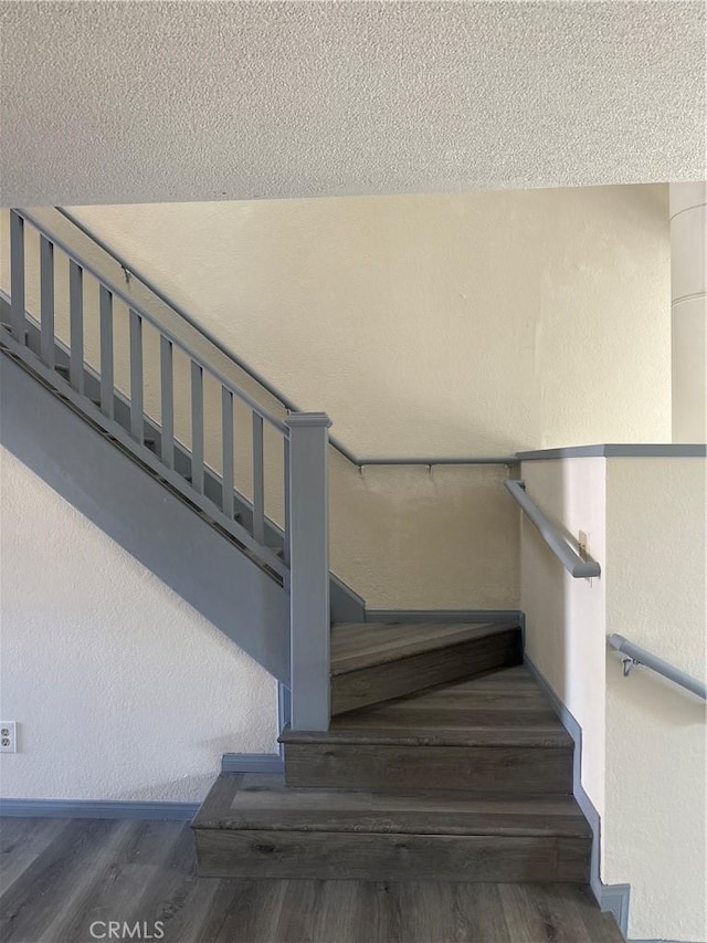 stairs featuring a textured wall, a textured ceiling, and wood finished floors