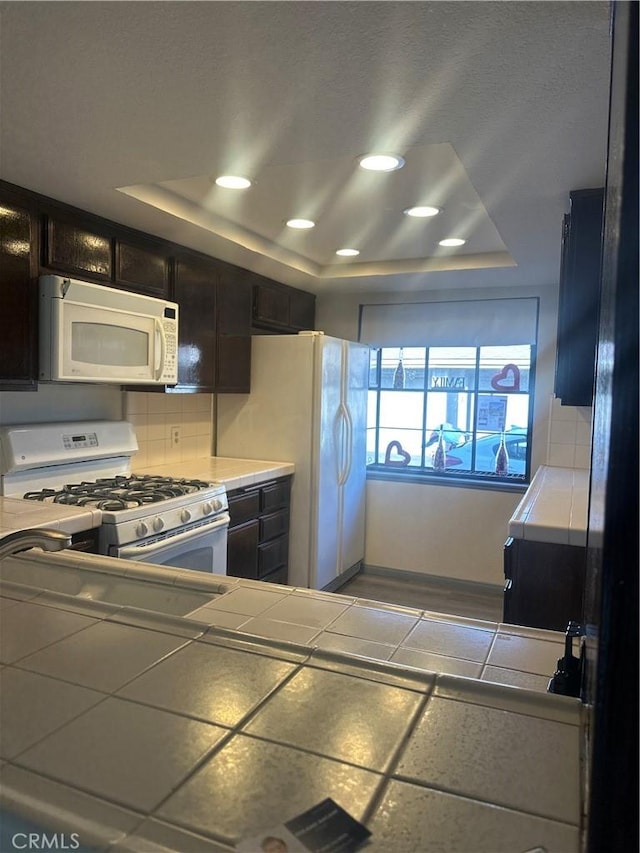 kitchen featuring tile countertops, a tray ceiling, white appliances, and backsplash