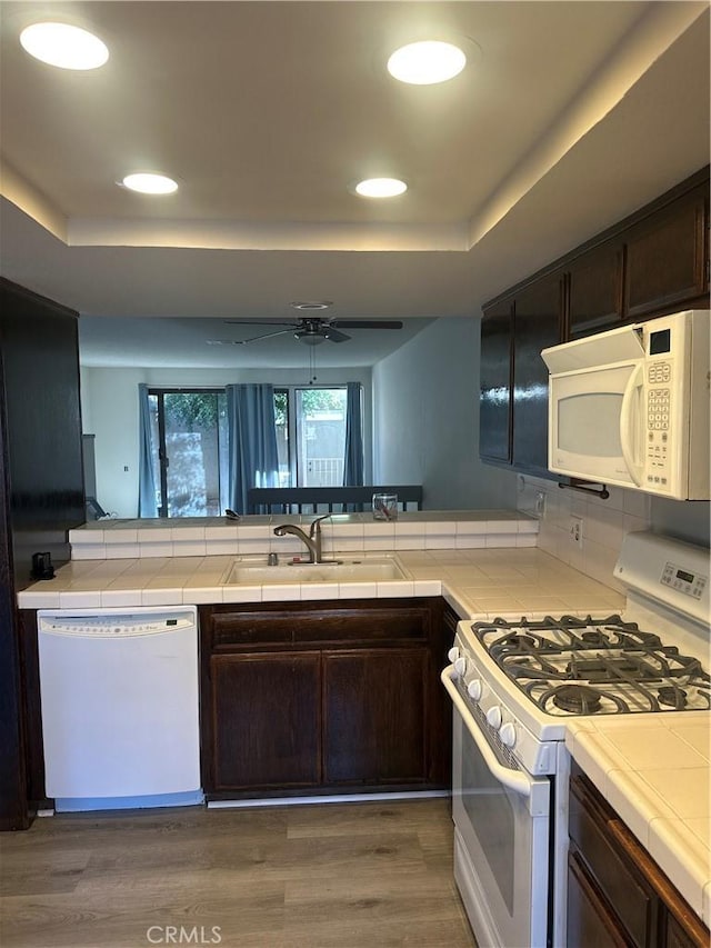 kitchen featuring tile countertops, white appliances, a raised ceiling, and dark brown cabinets