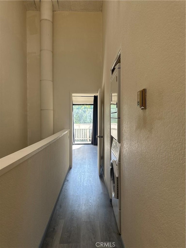 hallway with stacked washer / dryer, dark wood-style flooring, and a high ceiling