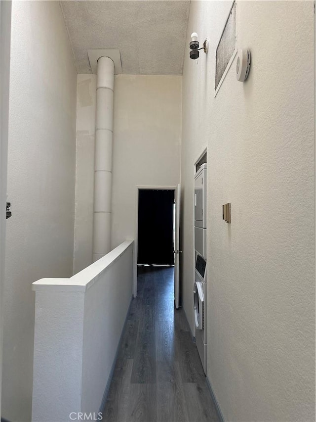 hall featuring dark wood-style flooring, stacked washer and clothes dryer, and an upstairs landing