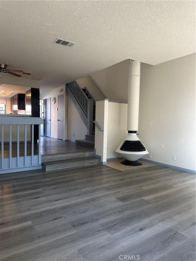 unfurnished living room featuring a ceiling fan, visible vents, stairway, and wood finished floors