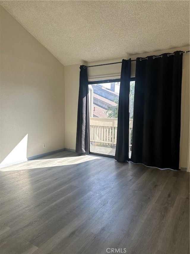 empty room featuring vaulted ceiling, a textured ceiling, and wood finished floors