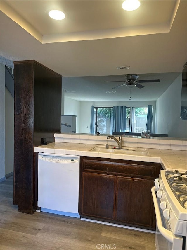 kitchen featuring white appliances, wood finished floors, dark brown cabinets, tile counters, and a raised ceiling