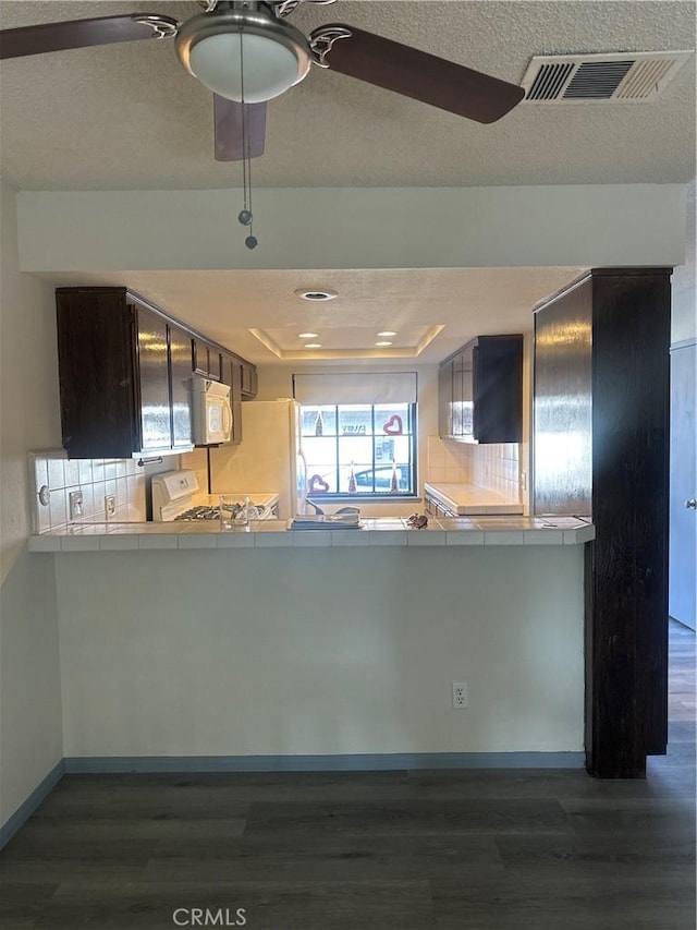 kitchen with white appliances, visible vents, a raised ceiling, tile countertops, and dark wood-style flooring