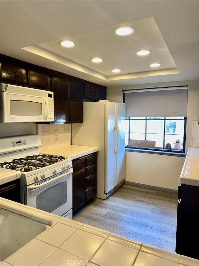 kitchen featuring white appliances, a tray ceiling, light countertops, and light wood-style floors